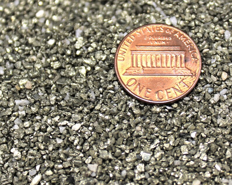 May include: A close-up of a US penny coin resting on a bed of small, metallic, gray-colored rocks. The coin features the Lincoln Memorial and the inscription "United States of America, E Pluribus Unum, One Cent".