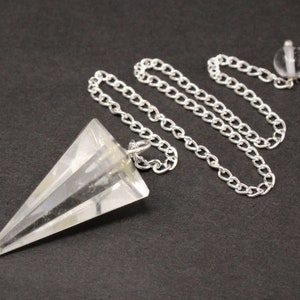 May include: A clear quartz crystal pendulum with a silver chain. The pendulum is shaped like a pyramid with a pointed tip. The chain is attached to a small silver ring at the top of the pendulum.