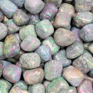 May include: A close-up of a collection of tumbled ruby zoisite stones. The stones are a mix of green, pink, and blue colors with a speckled pattern.