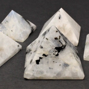 Puede incluir: Cinco peque&ntilde;as piedras en forma de pir&aacute;mide. Las piedras son blancas con inclusiones negras y grises. Las pir&aacute;mides se exhiben sobre una superficie gris oscuro. Las pir&aacute;mides son un objeto decorativo.