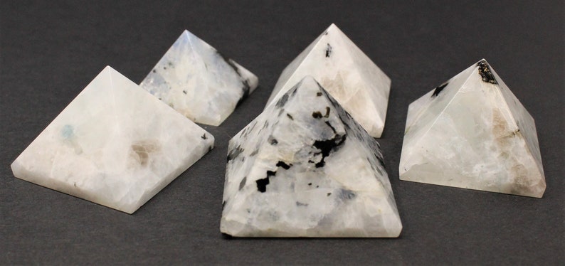 Puede incluir: Cinco peque&ntilde;as piedras en forma de pir&aacute;mide. Las piedras son blancas con inclusiones negras y grises. Las pir&aacute;mides se exhiben sobre una superficie gris oscuro. Las pir&aacute;mides son un objeto decorativo.