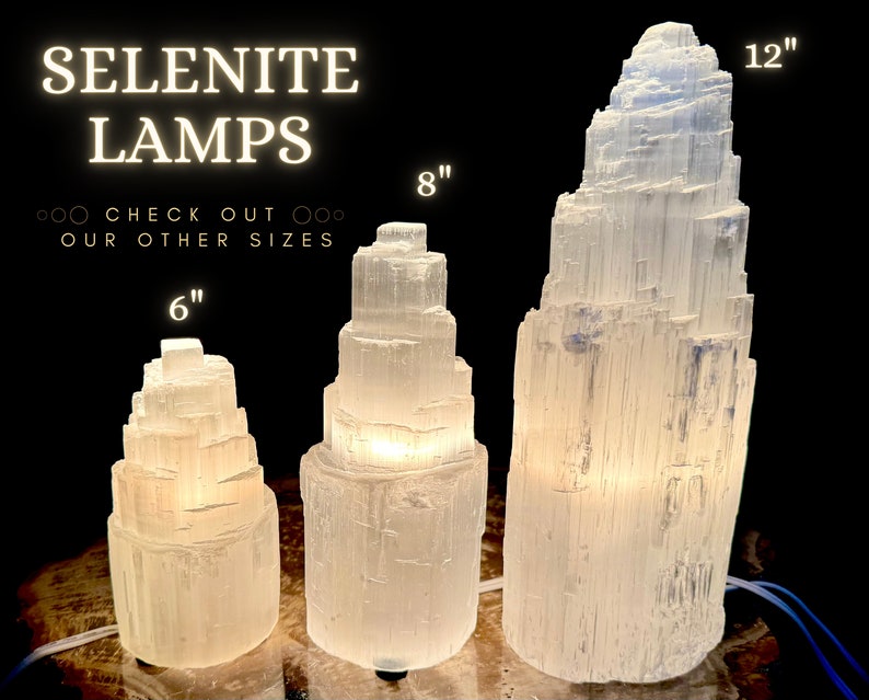 Może przedstawiać: Trzy podświetlane lampy z selenu o r&oacute;żnych rozmiarach: 15 cm, 20 cm i 30 cm wysokości. Lampy są białe i mają warstwową, krystaliczną strukturę. Tekst "SELENITE LAMPS" jest wyświetlany nad lampami.