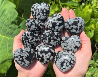 Puede incluir: Una colección de diez piedras de obsidiana copo de nieve en forma de corazón, de color negro y blanco. Las piedras son lisas y pulidas, con un patrón moteado.