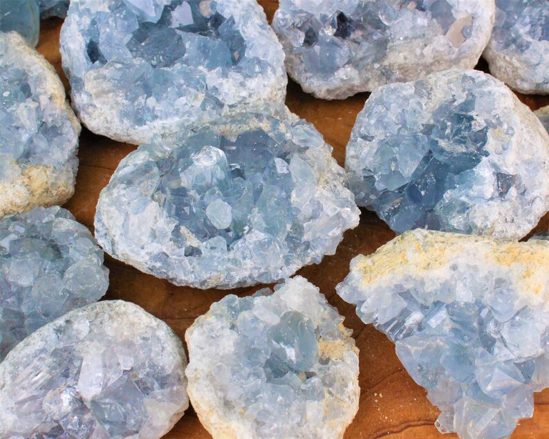 May include: A collection of blue celestite crystal clusters. The crystals are a light blue color and have a rough, natural texture. The clusters are various sizes and shapes.