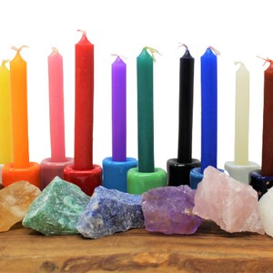 May include: A set of 10 colorful candles arranged in a row on a wooden surface with various crystals in front of each candle. The candles are in the colors of the rainbow, with the exception of black and white.