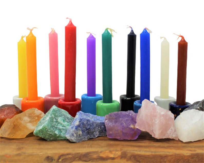 May include: A set of 10 colorful candles arranged in a row on a wooden surface with various crystals in front of each candle. The candles are in the colors of the rainbow, with the exception of black and white.
