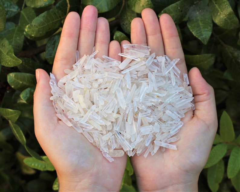 May include: A handful of small, clear quartz crystals, also known as rock crystals, in the shape of points. The crystals are held in the palms of a person's hands.