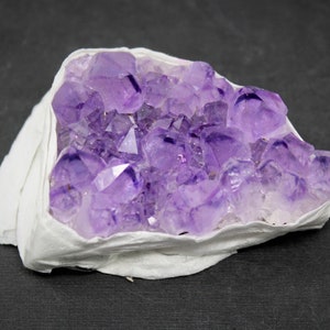 May include: A cluster of amethyst crystals in shades of purple, set in a white, natural matrix. The crystals are arranged in a natural formation, showcasing their unique shapes and facets.