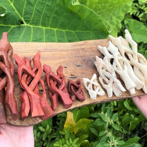 May include: A collection of carved wooden display stands arranged on a wooden board. The stands feature an interlocking, folding design and are available in two distinct finishes: a deep reddish-brown stain and a natural, light-colored wood tone.