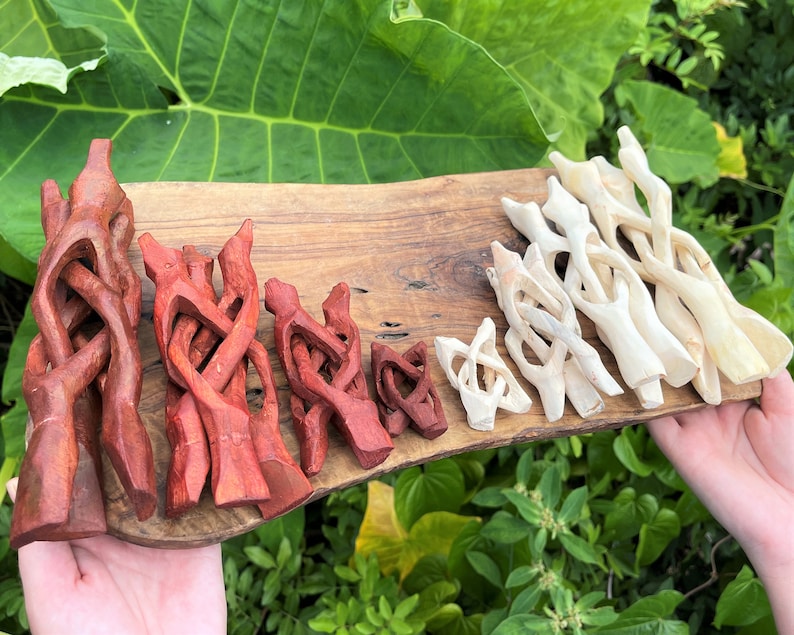 May include: A collection of carved wooden display stands arranged on a wooden board. The stands feature an interlocking, folding design and are available in two distinct finishes: a deep reddish-brown stain and a natural, light-colored wood tone.