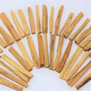 May include: A collection of approximately 40 natural Palo Santo sticks, arranged in a semi-circle on a white background. The sticks are light brown in color and have a rough, natural texture.