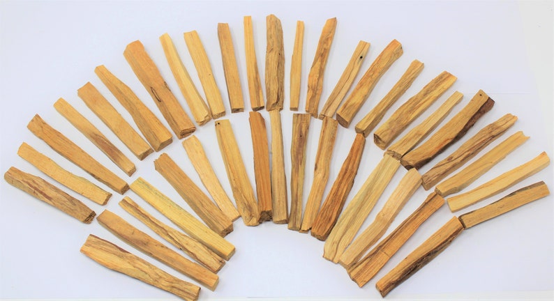 May include: A collection of approximately 40 natural Palo Santo sticks, arranged in a semi-circle on a white background. The sticks are light brown in color and have a rough, natural texture.