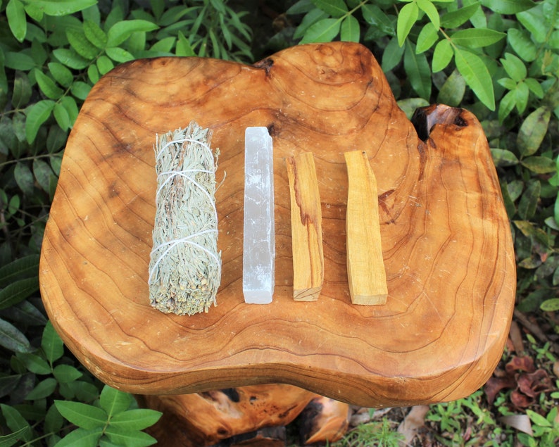 May include: A set of four smudging sticks on a wooden surface. The sticks are white, gray, brown, and light brown. The sticks are used for smudging ceremonies.