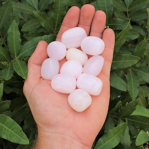 May include: A collection of smooth, pale pink tumbled stones. The stones are various sizes and shapes, and have a slightly translucent appearance.