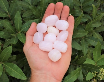 May include: A collection of smooth, pale pink tumbled stones. The stones are various sizes and shapes, and have a slightly translucent appearance.