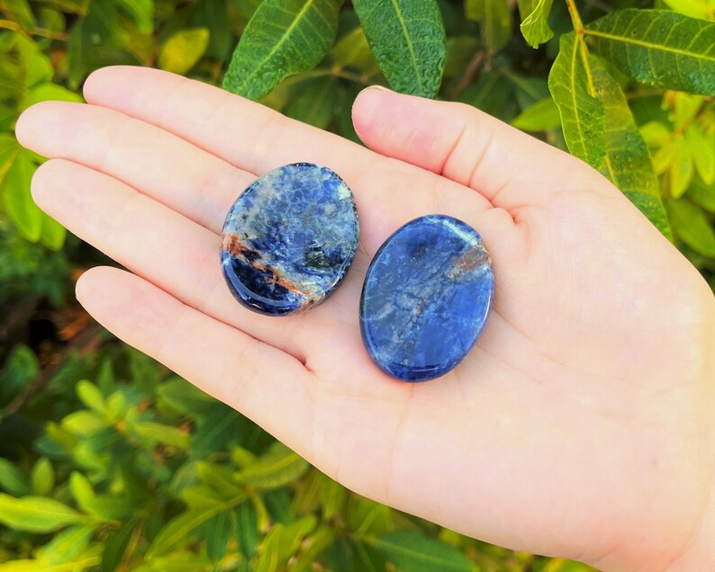 Op de afbeelding: Twee ovale, gepolijste stenen, een blauwe met witte en bruine markeringen, de andere een donkerdere blauwe met witte en bruine markeringen.