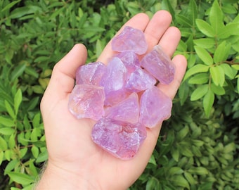 May include: A collection of amethyst crystals in various sizes and shapes, ranging from light to deep purple, displayed in a hand.