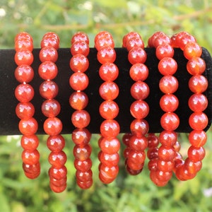 May include: Several bracelets with large, round, orange-red beads are displayed against a black background. The beads are strung together, creating a continuous loop. The bracelets are likely made of a gemstone or similar material.