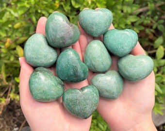 Puede incluir: Una colección de diez piedras verdes en forma de corazón. Las piedras son lisas y pulidas, y están dispuestas en una mano.