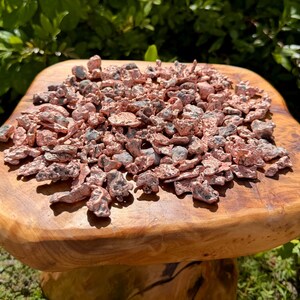 May include: A collection of small, irregular copper nuggets with a metallic, reddish-brown finish and dark, textured inclusions. The pieces vary in shape and size, displaying a raw, unrefined appearance with a bright, reflective surface quality.