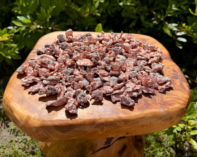 May include: A collection of small, irregular copper nuggets with a metallic, reddish-brown finish and dark, textured inclusions. The pieces vary in shape and size, displaying a raw, unrefined appearance with a bright, reflective surface quality.