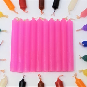 May include: A set of 12 pink candle sticks. The candles are arranged in a row on a white surface.