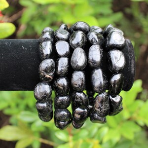 May include: A bracelet composed of multiple strands of polished, irregular black tourmaline gemstone beads. The beads have a glossy, reflective surface and are strung together to form a continuous, rounded shape with a dark, opaque appearance.