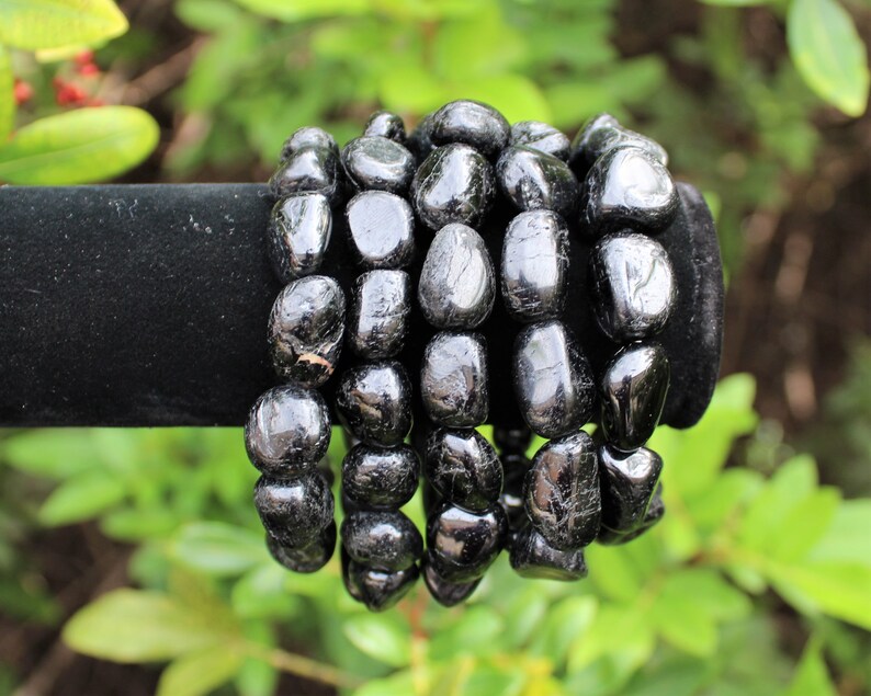 May include: A bracelet composed of multiple strands of polished, irregular black tourmaline gemstone beads. The beads have a glossy, reflective surface and are strung together to form a continuous, rounded shape with a dark, opaque appearance.