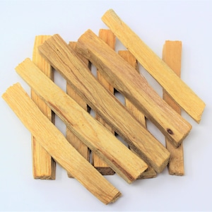 May include: A selection of light brown Palo Santo wood sticks, arranged on a white background. The rectangular sticks display visible wood grain and varying shades of tan and beige. The image is well-lit, emphasizing the natural texture and colour of the wood.