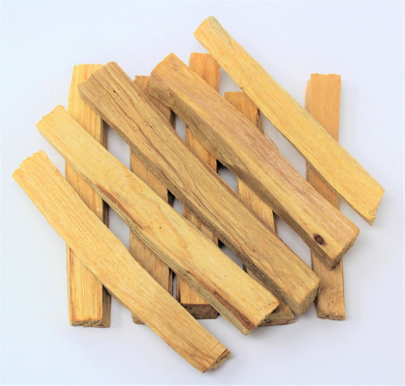 May include: A selection of light brown Palo Santo wood sticks, arranged on a white background. The rectangular sticks display visible wood grain and varying shades of tan and beige. The image is well-lit, emphasizing the natural texture and colour of the wood.