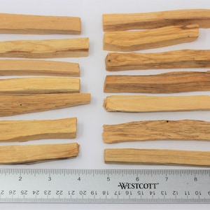 May include: Several rectangular Palo Santo wood sticks, light brown in colour, are arranged on a white surface. A ruler with inch measurements is placed below the sticks. The wood pieces have a natural, textured appearance.