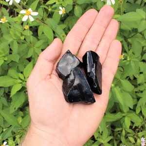 Puede incluir: Tres piezas de obsidiana negra, un tipo de vidrio volc&aacute;nico, se sostienen en una mano. La obsidiana es oscura y brillante.