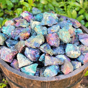 May include: A dark wooden bucket filled with numerous raw chalcopyrite mineral stones. The stones exhibit a metallic luster with iridescent, multi-colored surfaces featuring shades of blue, purple, gold, and green across their jagged, uneven textures.