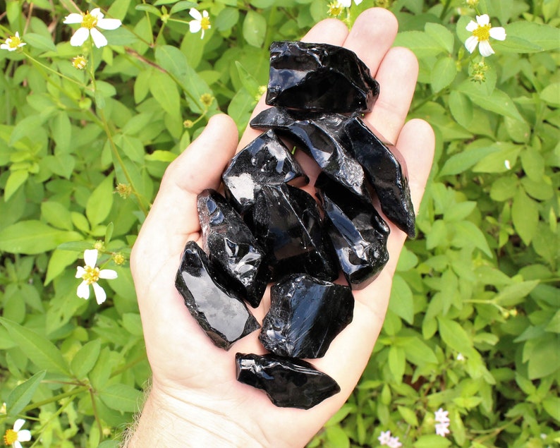Puede incluir: Un pu&ntilde;ado de piedras de obsidiana negra, tambi&eacute;n conocidas como vidrio volc&aacute;nico, con bordes afilados y un acabado brillante.