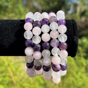 May include: Three stacked bracelets made of amethyst, rose quartz, and clear quartz beads. The bracelets are all the same size and have a polished finish.