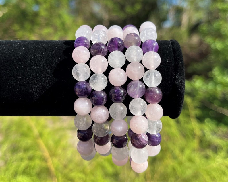 May include: Three stacked bracelets made of amethyst, rose quartz, and clear quartz beads. The bracelets are all the same size and have a polished finish.