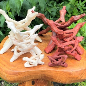 May include: A collection of carved wooden display stands in two distinct groups. One group features a light, natural wood finish, while the other group is stained in a deep reddish-brown tone. Each stand has a multi-legged, interlocking design.