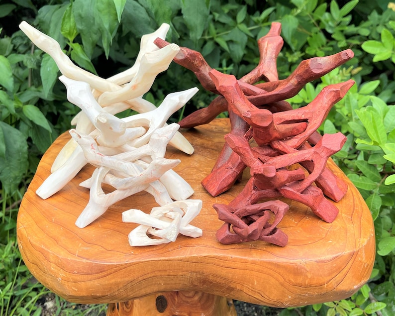 May include: A collection of carved wooden display stands in two distinct groups. One group features a light, natural wood finish, while the other group is stained in a deep reddish-brown tone. Each stand has a multi-legged, interlocking design.