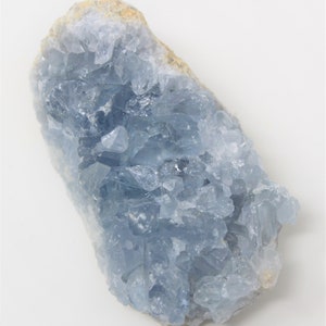 May include: A large, light blue celestite crystal cluster with a rough, natural surface. The crystal has a translucent appearance and is composed of many small, pointed crystals.