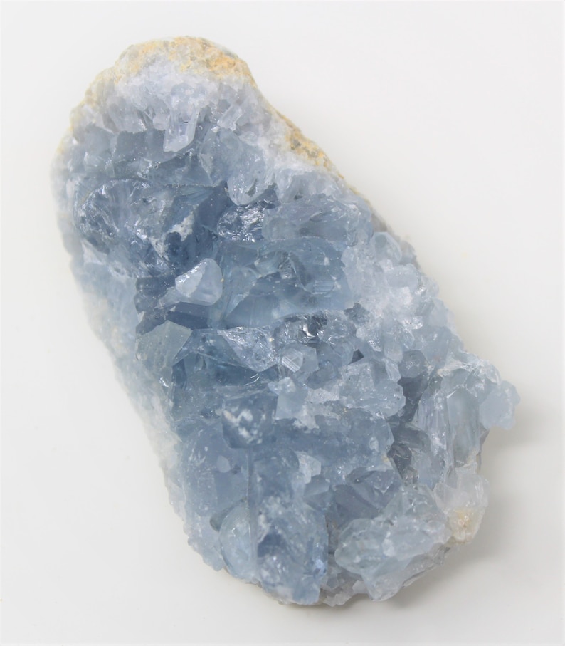 May include: A large, light blue celestite crystal cluster with a rough, natural surface. The crystal has a translucent appearance and is composed of many small, pointed crystals.