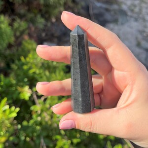 May include: Black obsidian crystal point, a dark, pointed stone with a smooth, polished surface.