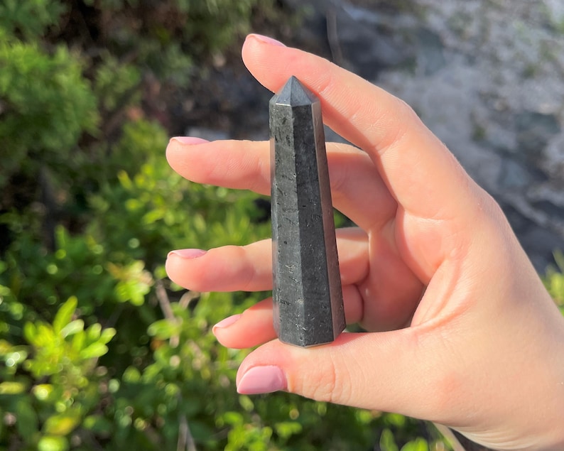 May include: Black obsidian crystal point, a dark, pointed stone with a smooth, polished surface.