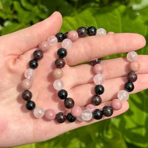 May include: Two bracelets made with pink, black, and brown beads. The bracelets are made with natural stones.
