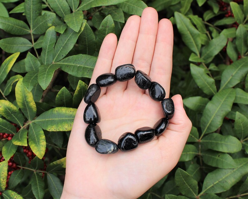 May include: A stretch bracelet composed of smooth, polished black tourmaline gemstone beads. The beads are irregular, rounded, and glossy, strung together in a circular loop to form a continuous band that fits around the wrist.