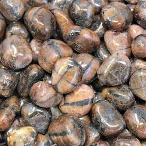 May include: A close-up view of a pile of brown and black striped tumbled stones. The stones are smooth and polished, with a variety of shapes and sizes.