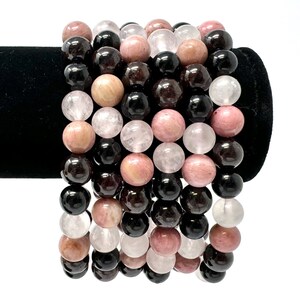 May include: A set of six bracelets made with natural gemstone beads. The bracelets feature black, pink, and white beads.