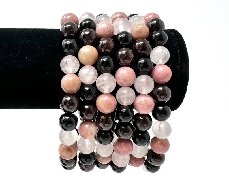 May include: A set of six bracelets made with natural gemstone beads. The bracelets feature black, pink, and white beads.