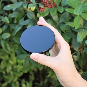 May include: A black round disc with a smooth, glossy surface. The disc is being held in a hand.