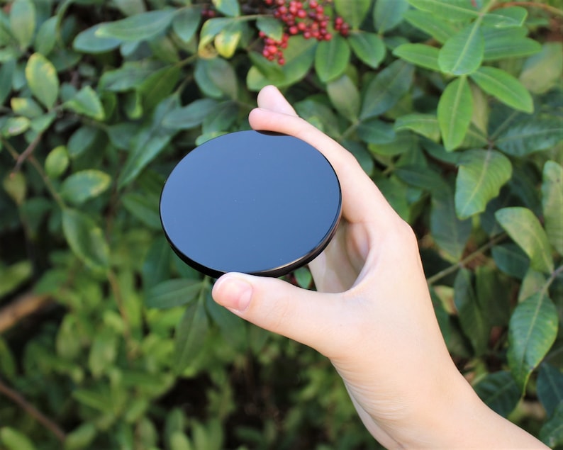 May include: A black round disc with a smooth, glossy surface. The disc is being held in a hand.