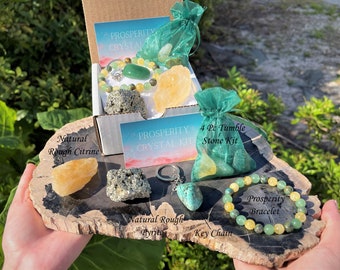 May include: A crystal kit with a variety of stones, a bracelet, and a keychain. The kit includes a natural rough citrine, pyrite, and a 4-piece tumble stone kit. The bracelet is labeled "Prosperity Bracelet". The kit is presented on a wooden surface.